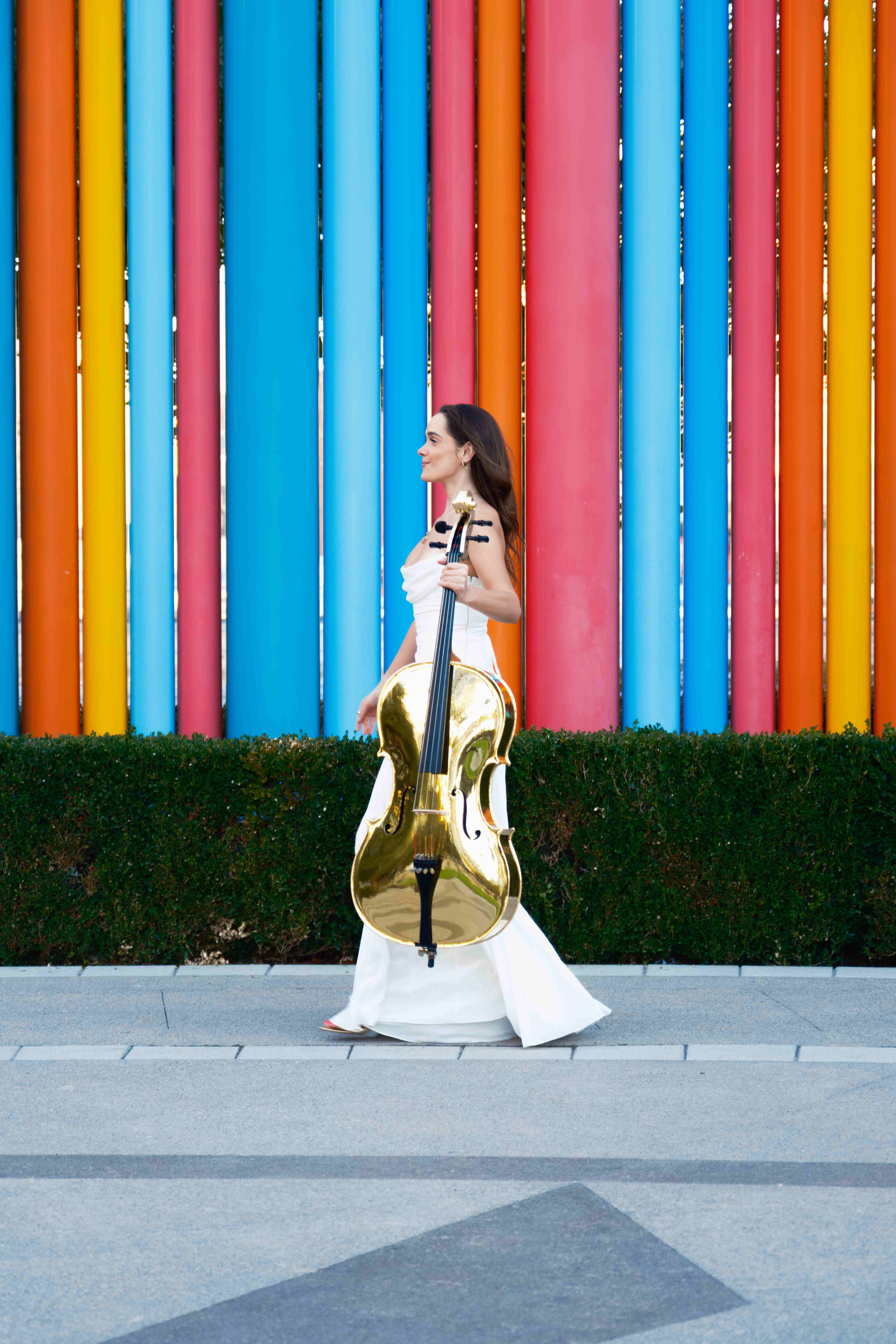 Elegant pose with golden cello against colorful striped backdrop